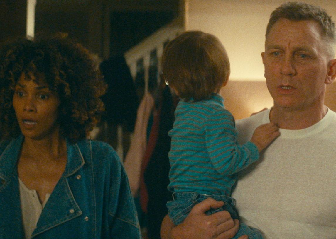 Daniel Craig, holding a small boy in his arms, stands next to Halle Berry, both of them looking scared.
