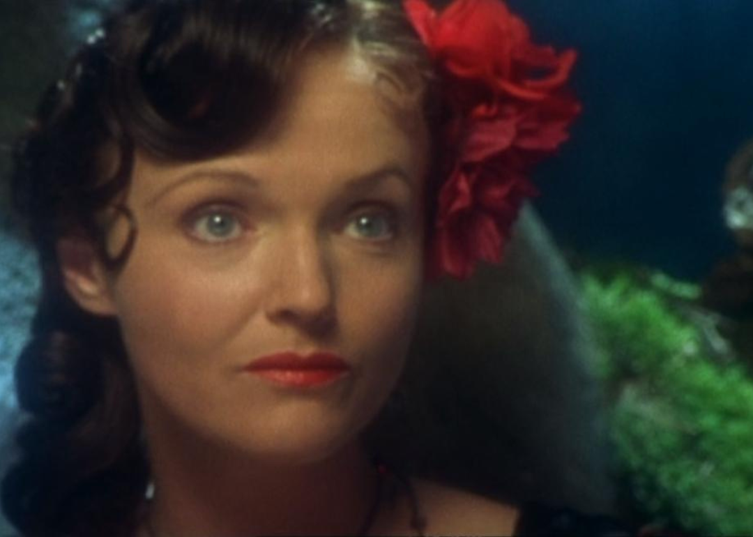 A dark-haired woman with a red bow in her hair.