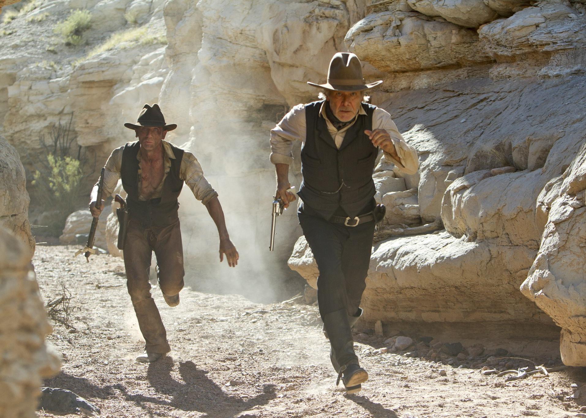 Harrison Ford and Daniel Craig dressed as cowboys running.