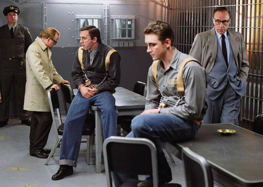 Peter Bogdanovich, Daniel Craig, Toby Jones, and Lee Pace talk in a jail cell with a guard watching.