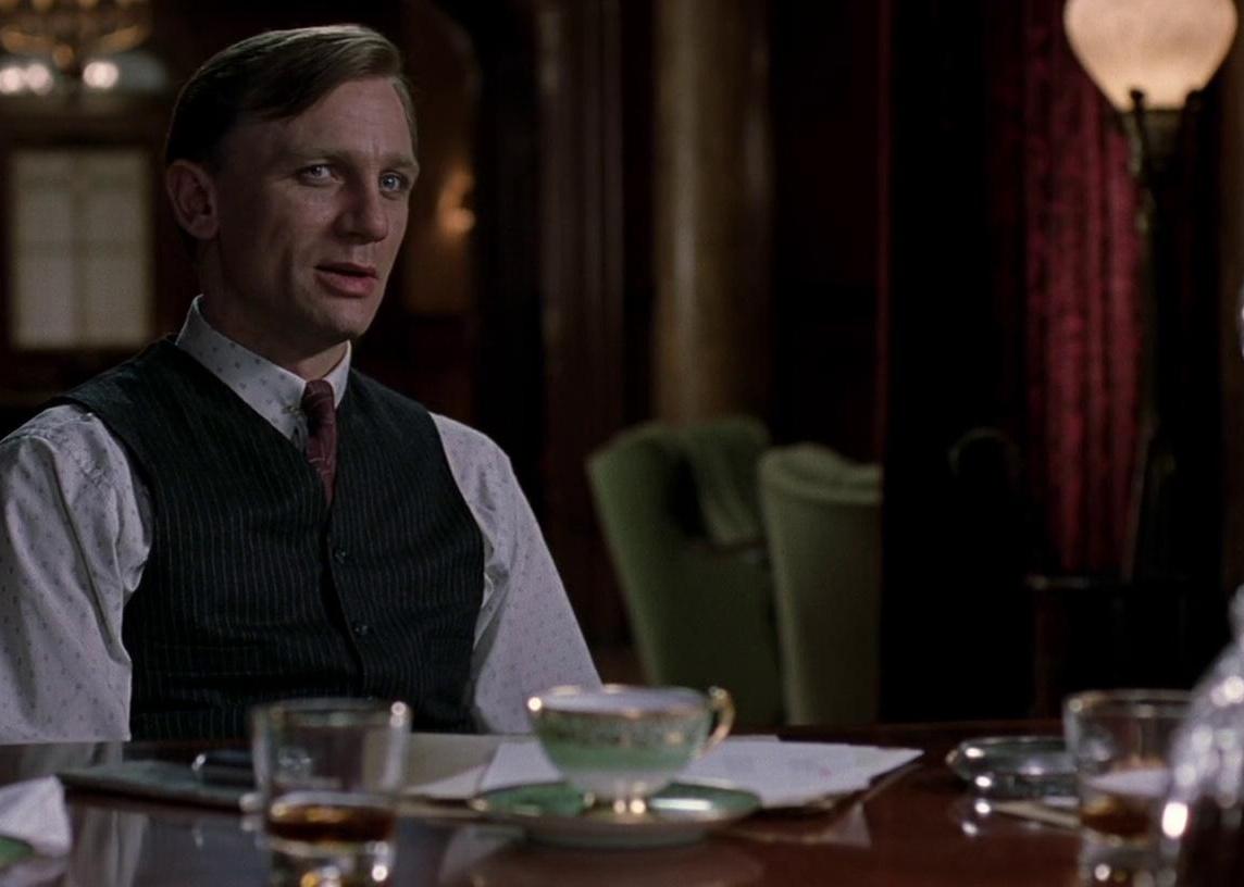 Daniel Craig in a pinstripe vest at a nice dining room table.