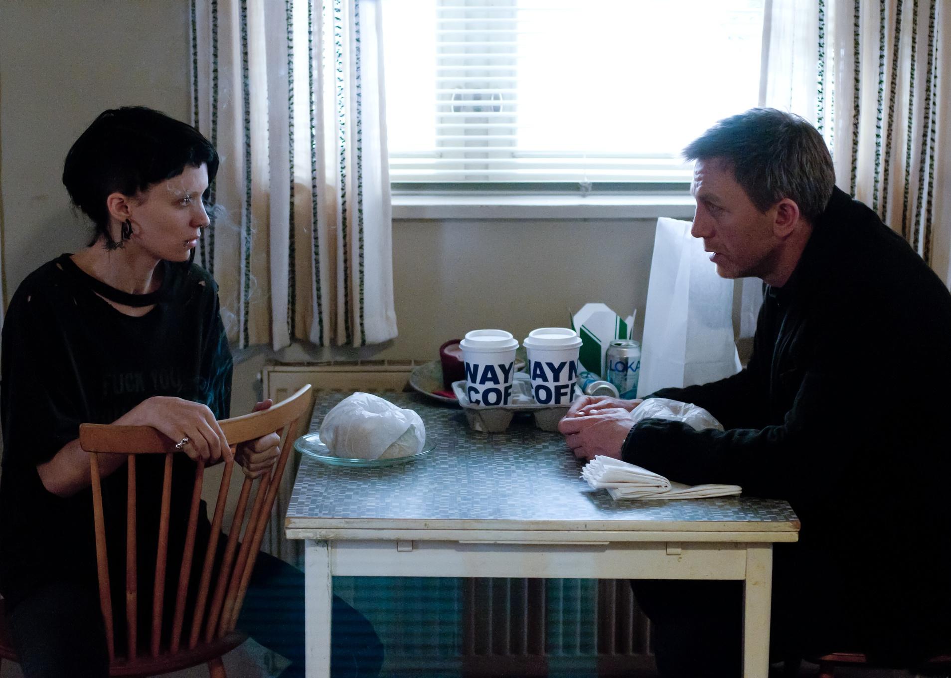 Daniel Craig and Rooney Mara sit at a small table together with coffee.