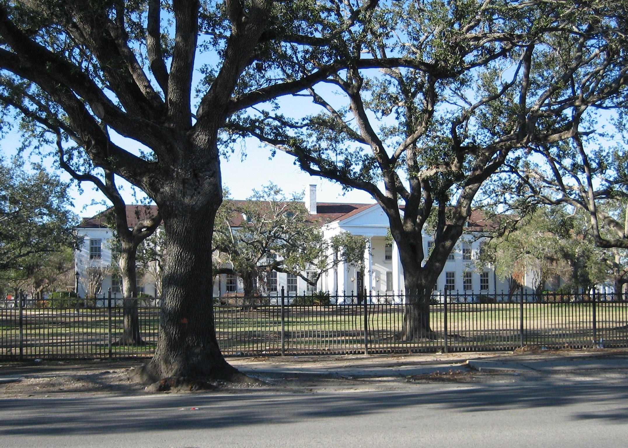 A large historic white building with an iron fence around the perimiter.