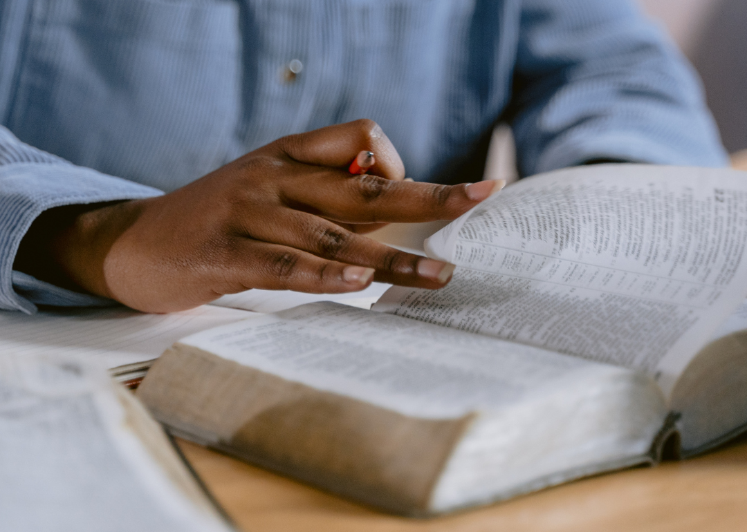 A student reading through a bible with a notebook and pencil.