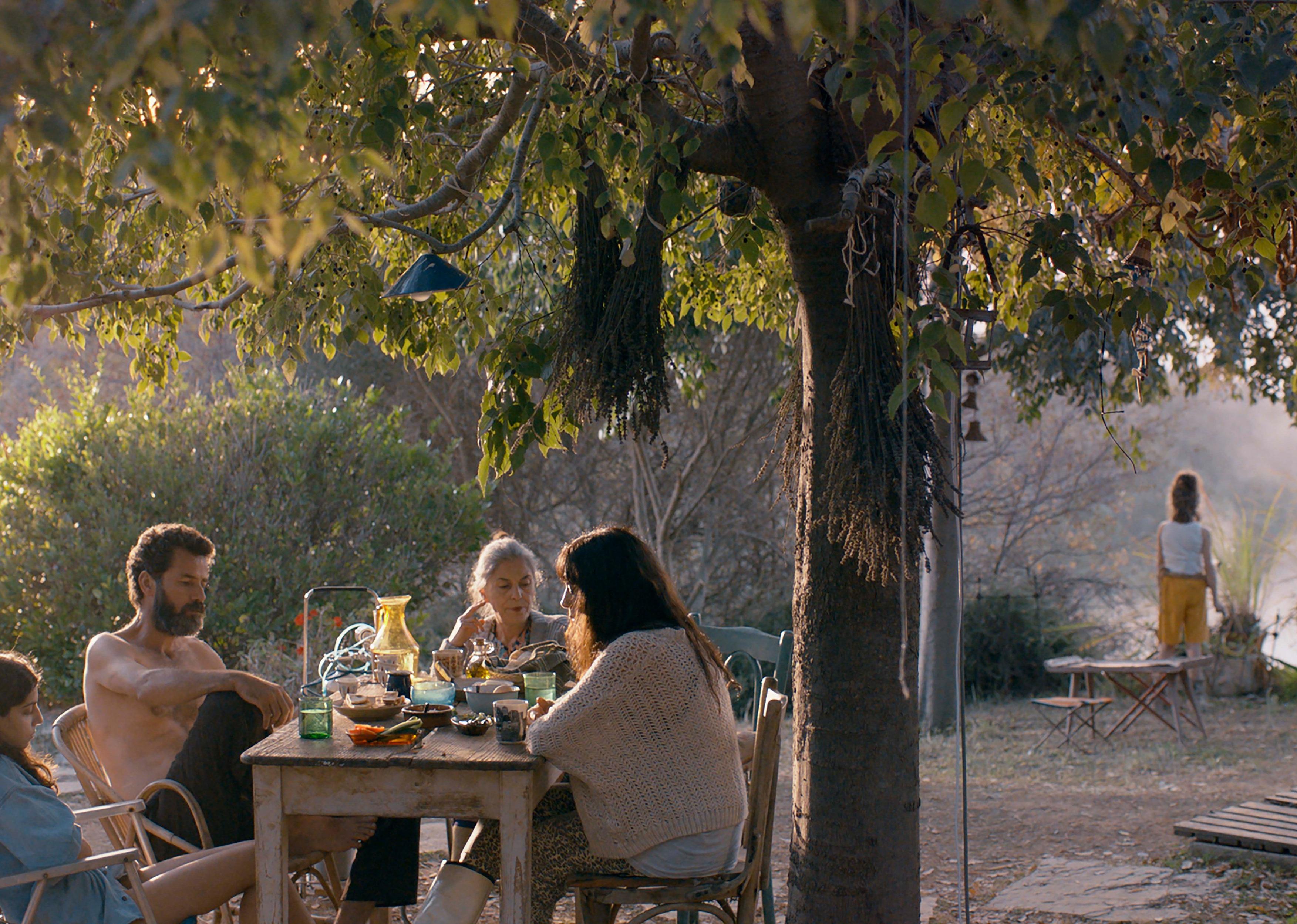 A family eating at a wooden table outside under a tree.