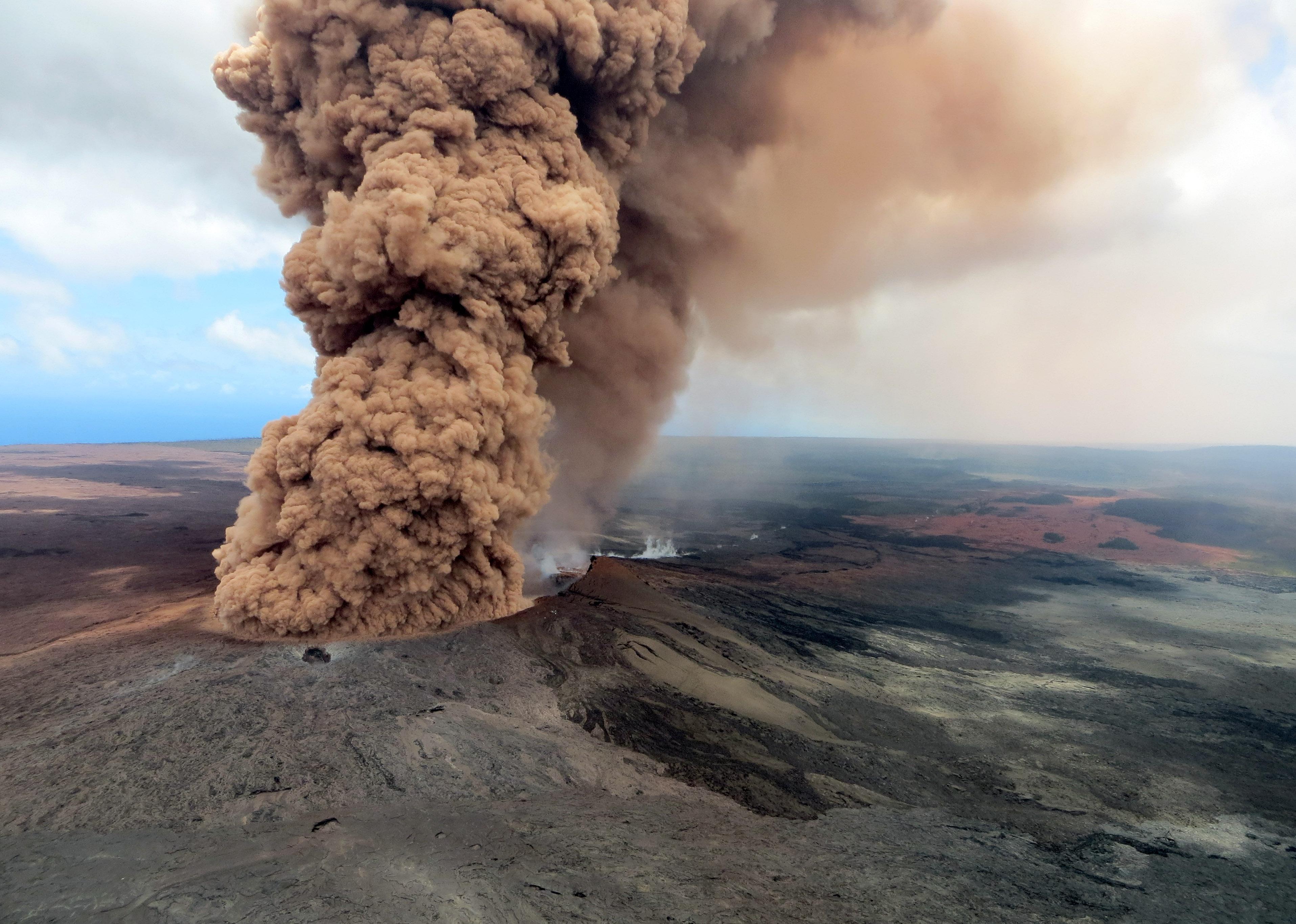 A column of reddish-brown ash plume from the eruption of Hawaii's Kilauea volcano rises high above the volcano.