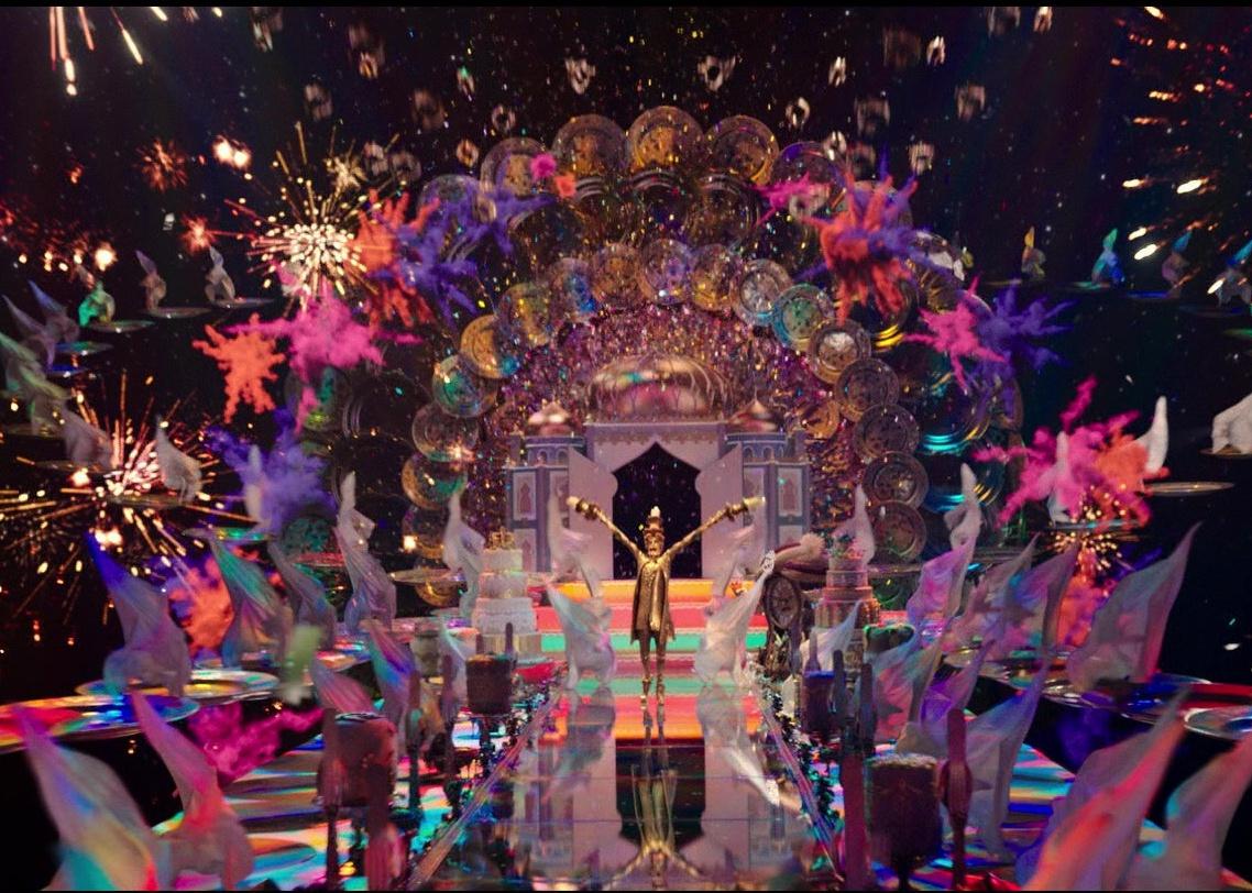 A man in gold on a shiny runway with colors bursting everywhere.
