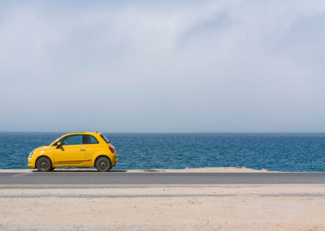 A yellow Fiat 500 by the ocean.