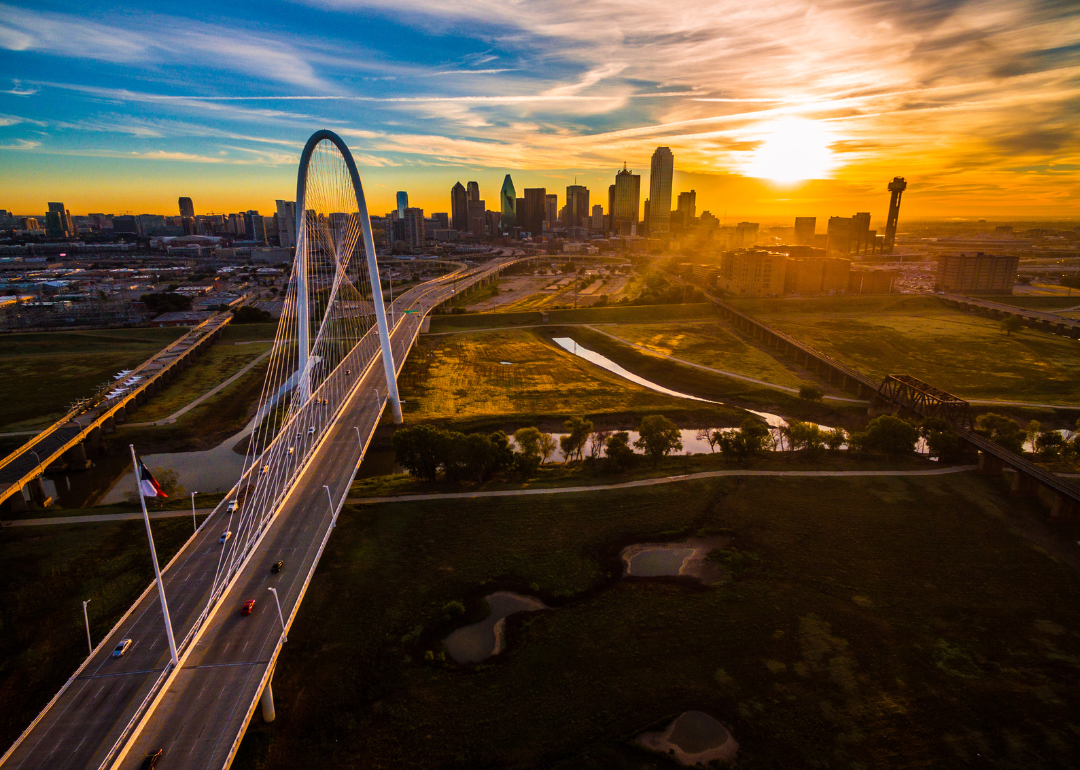 Cars on a large bridge with the Dallas skyline and sun setting in the background.