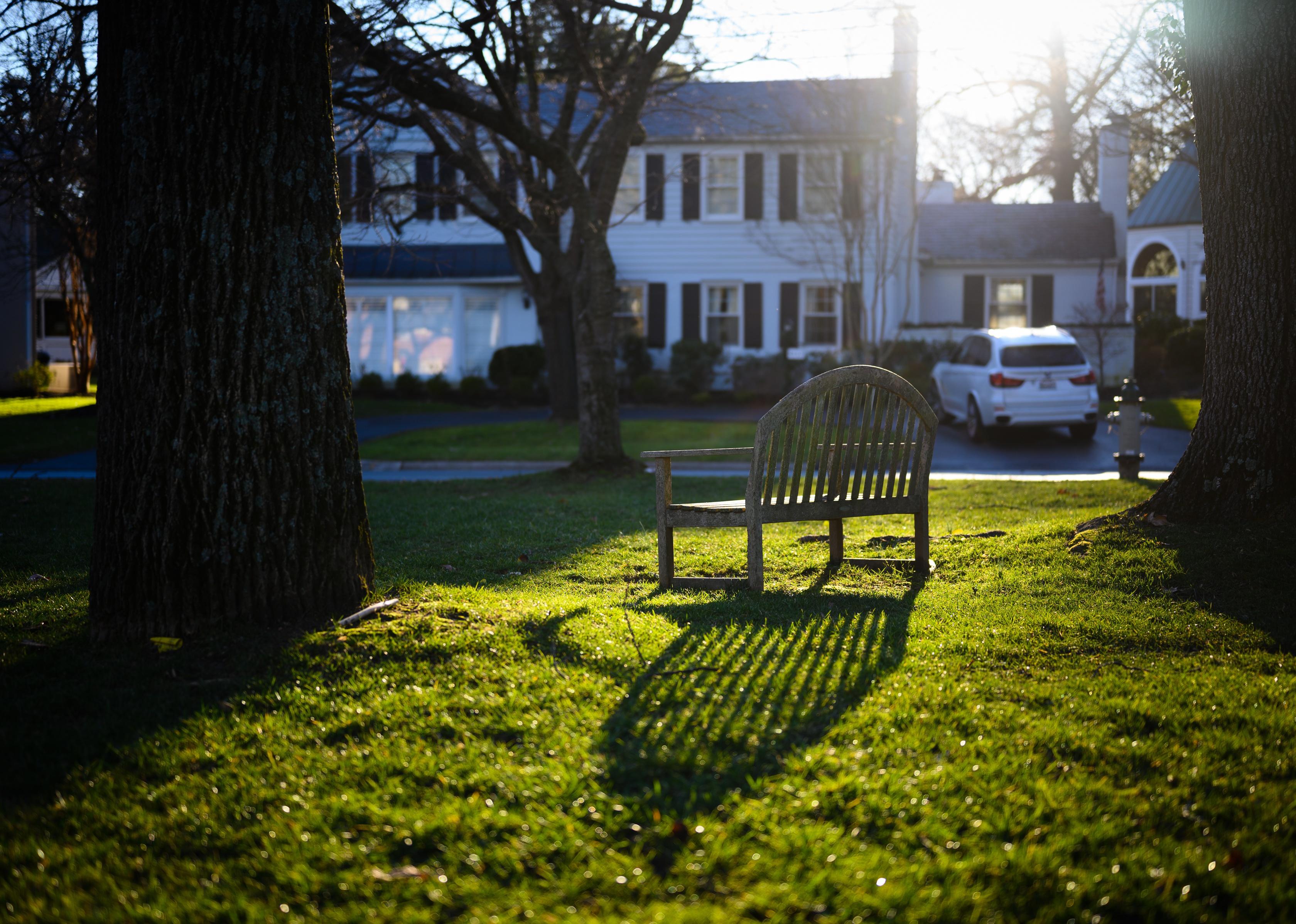 A wooden park bench in the green grass near historic homes.