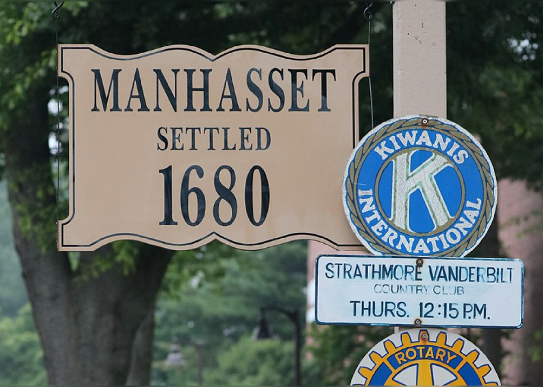 A historic Manhasset sign that says settled 1680 next to a Kiwanis International sign.