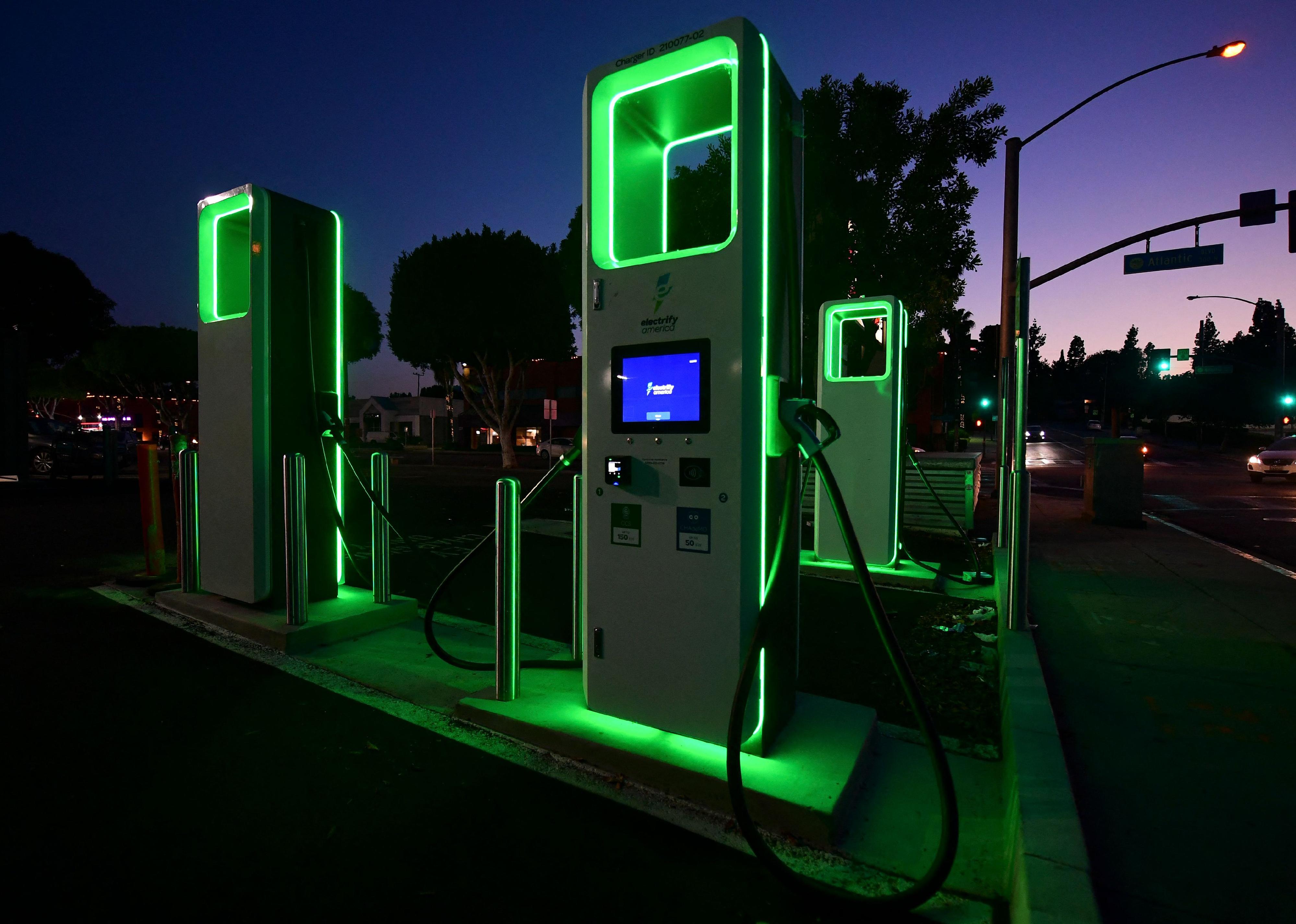 Electric vehicle charging station lit up in neon green at night.