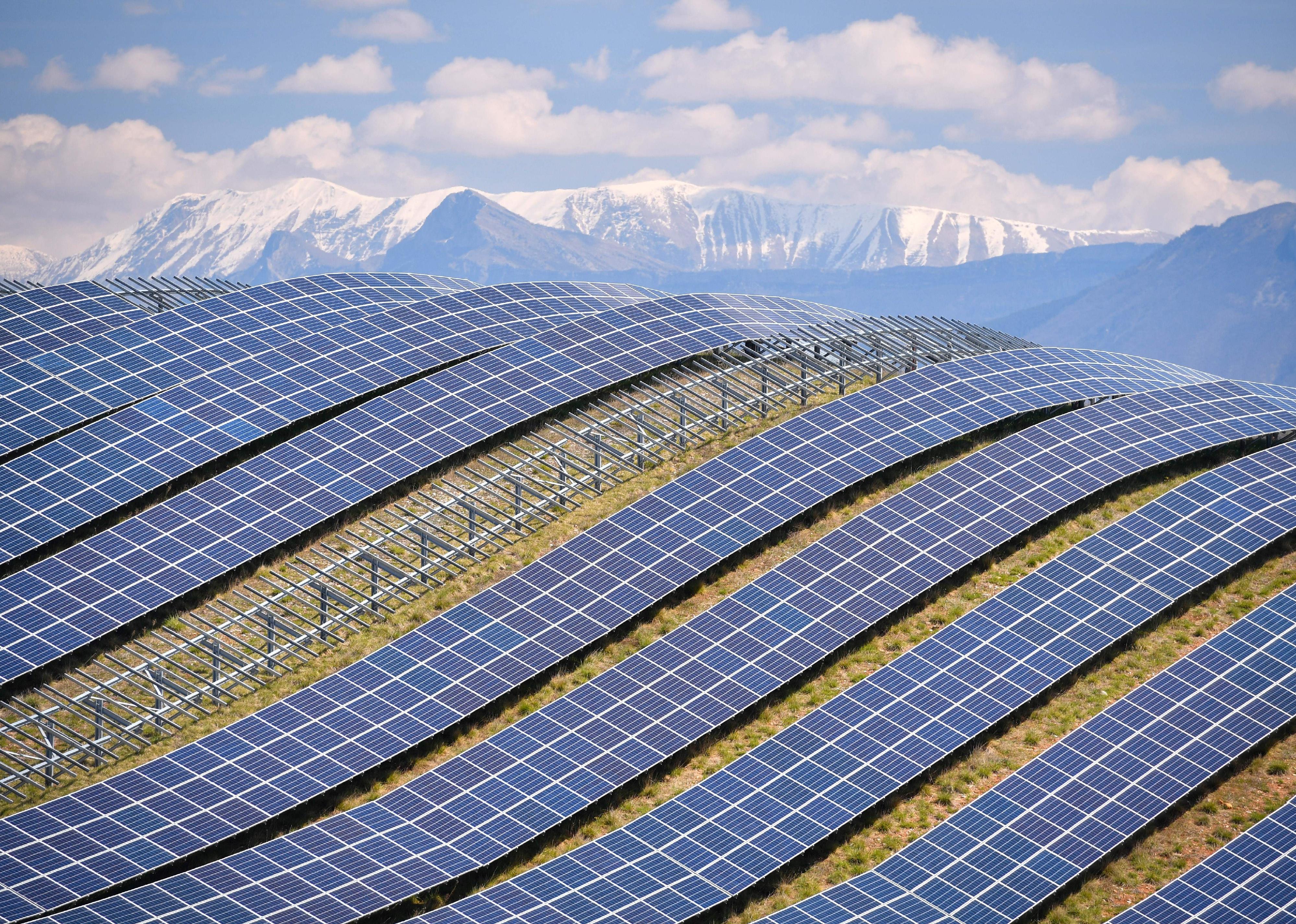Hills lined with solar panels with the snowy Alps in the background.