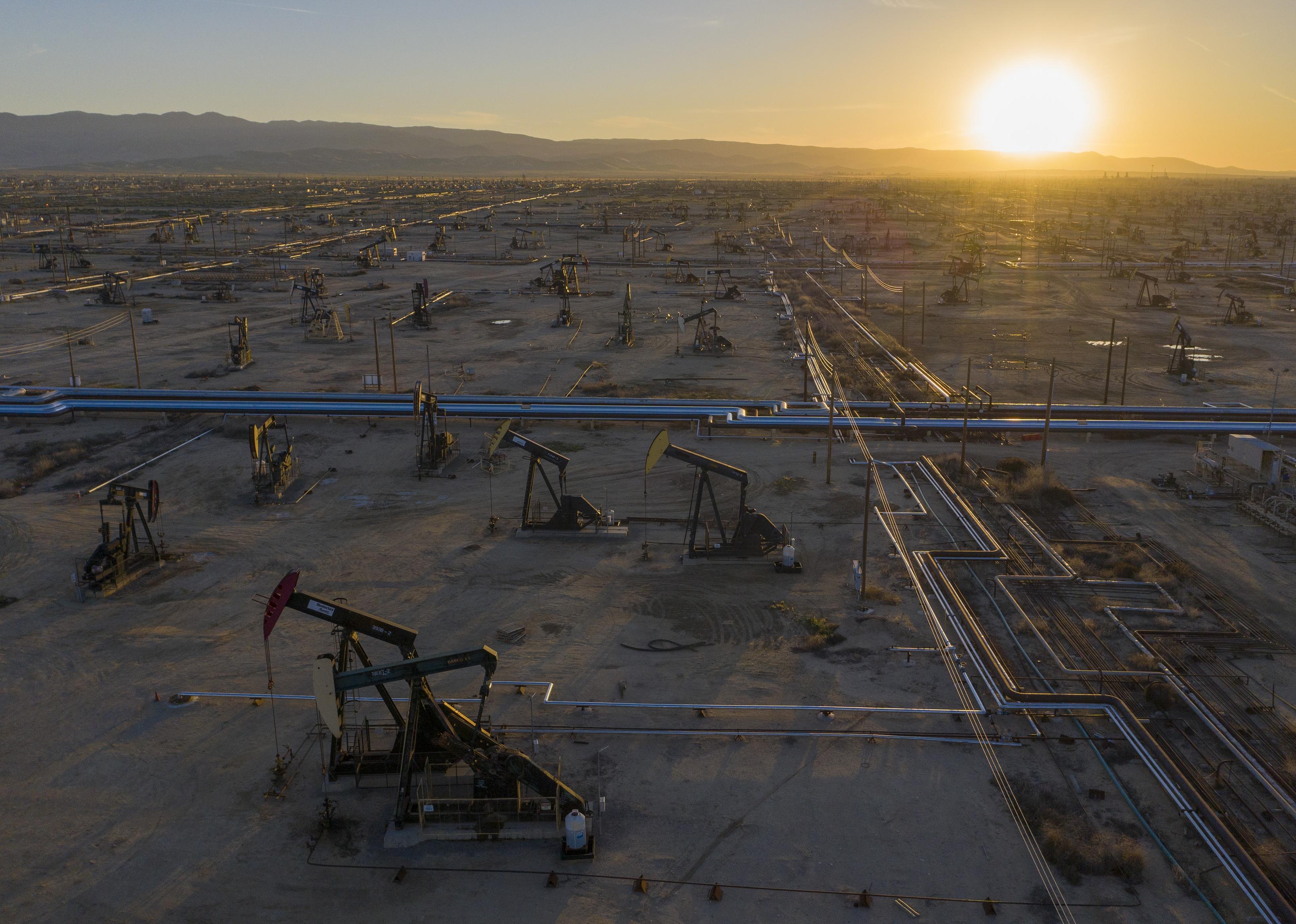 A massive oil field of pumpjacks and pipelines in California with mountains in the background.