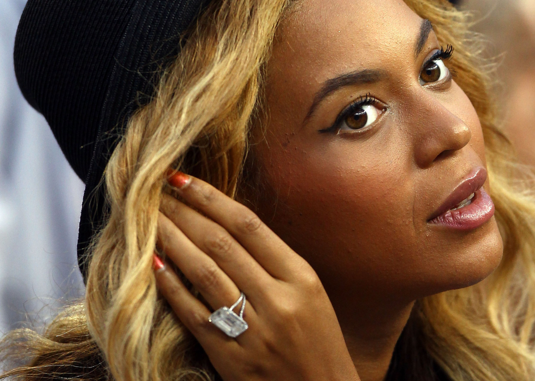 Beyonce wearing a black hat and holding her hand up to her ear showing her ring.