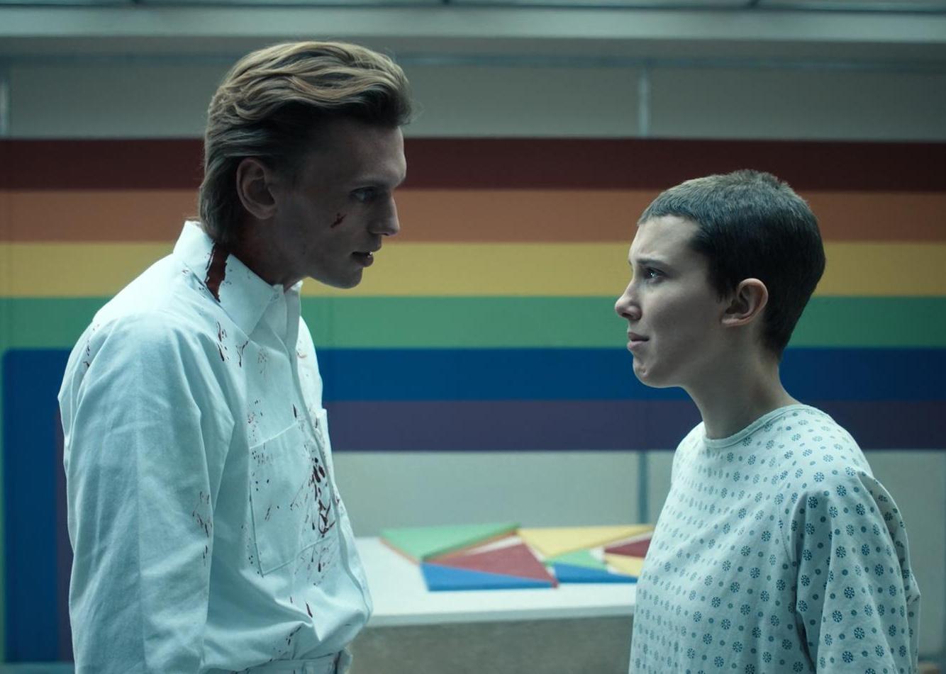Millie Bobby Brown, in a hospital gown, cries to a young man in a white coat.