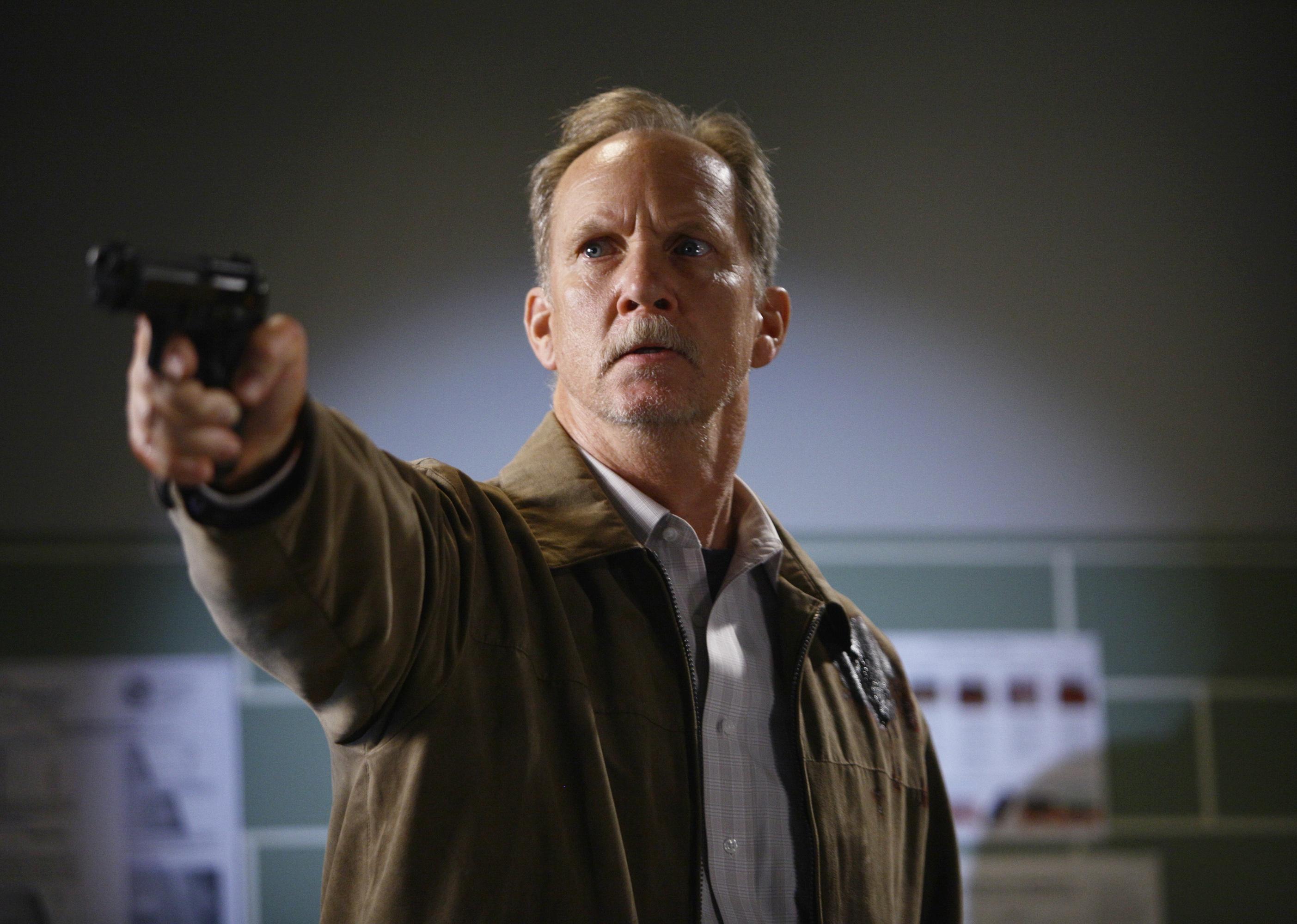 A man in a brown jacket pointing a gun.