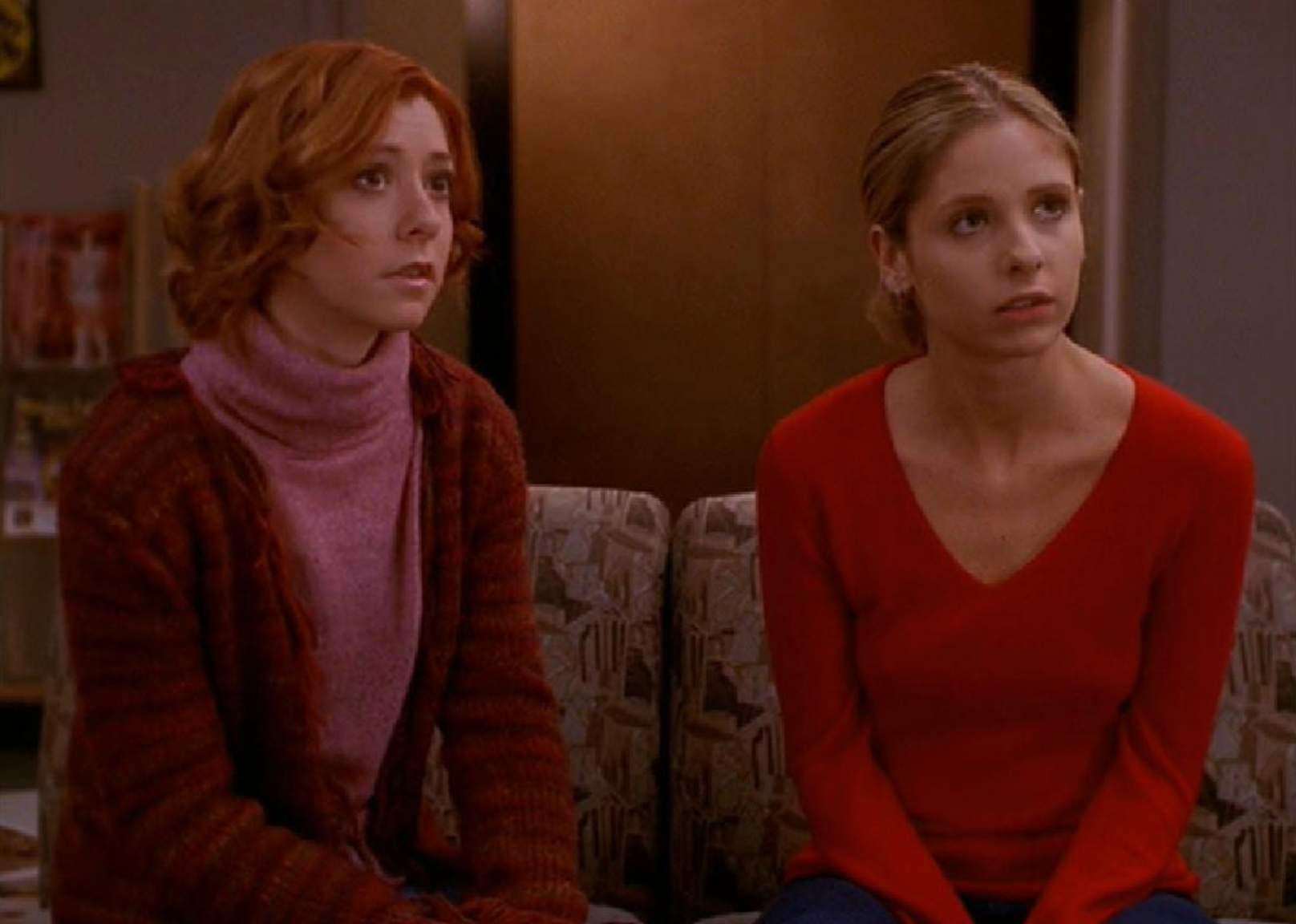Sarah Michelle Gellar and Alyson Hannigan, wearing pink and red, sit on the couch together.