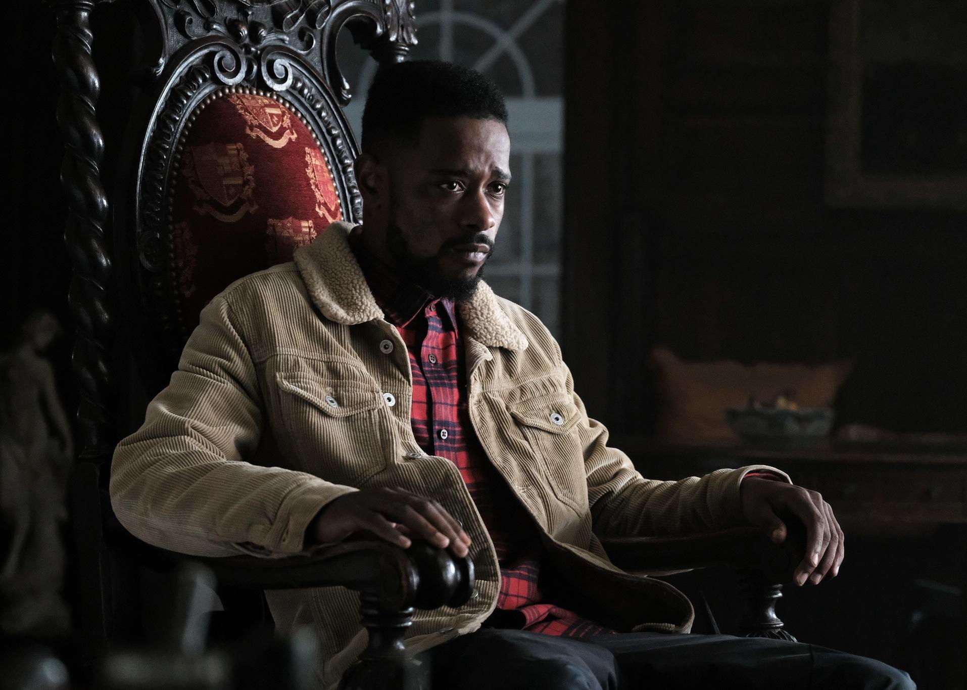A man in a red plaid shirt and tan corduroy jacket sits in a throne-like chair.