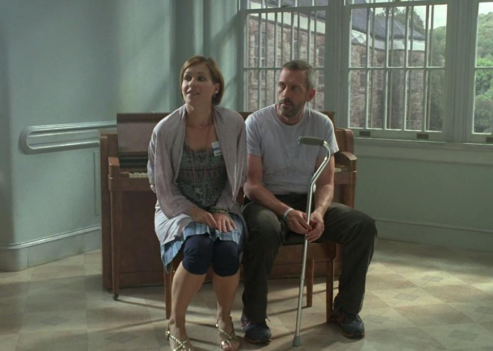 Hugh Laurie sits on a piano bench with a woman.