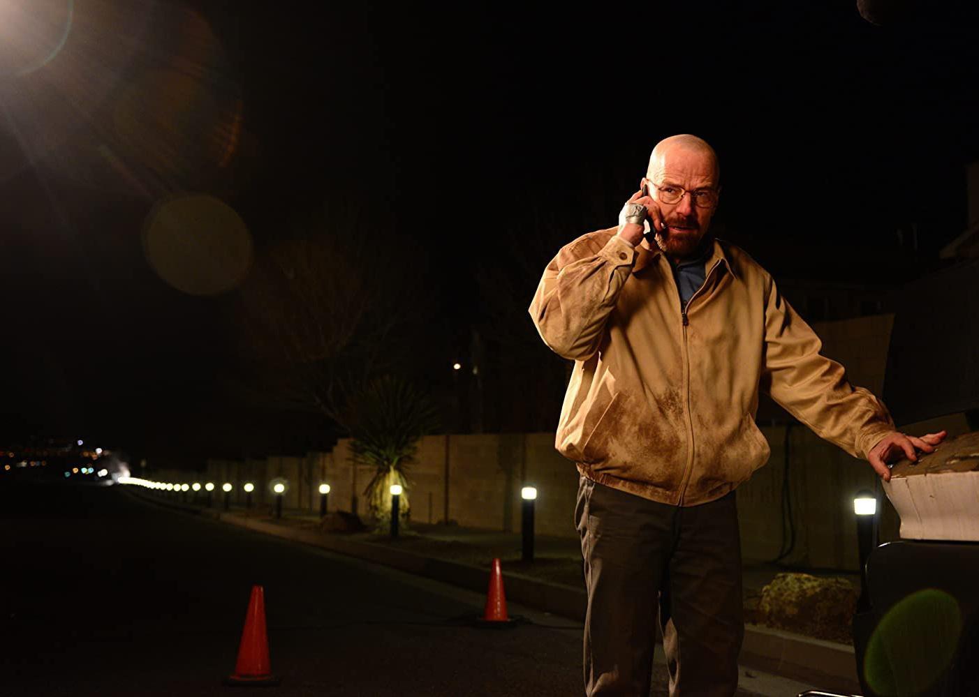 Bryan Cranston in a dirty jacket outside at night.