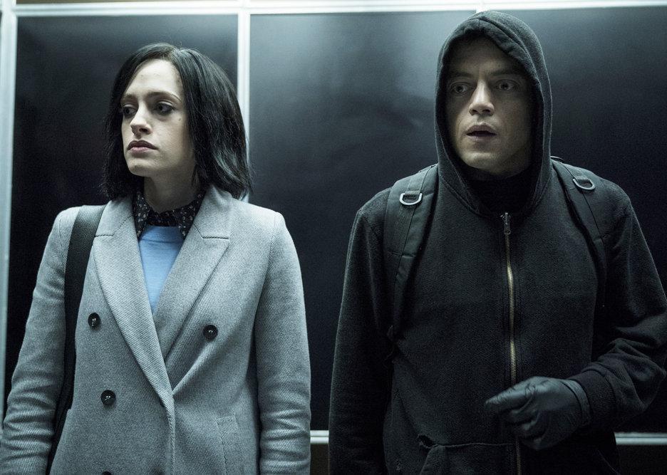 A man in a black hoodie stands next to a woman in an elevator.