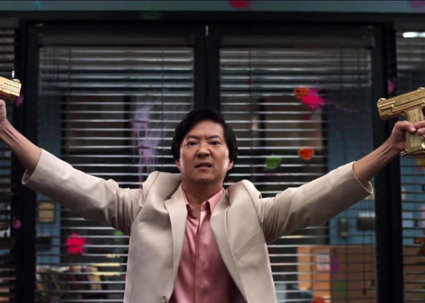 Ken Jeong holding two gold guns in the air.
