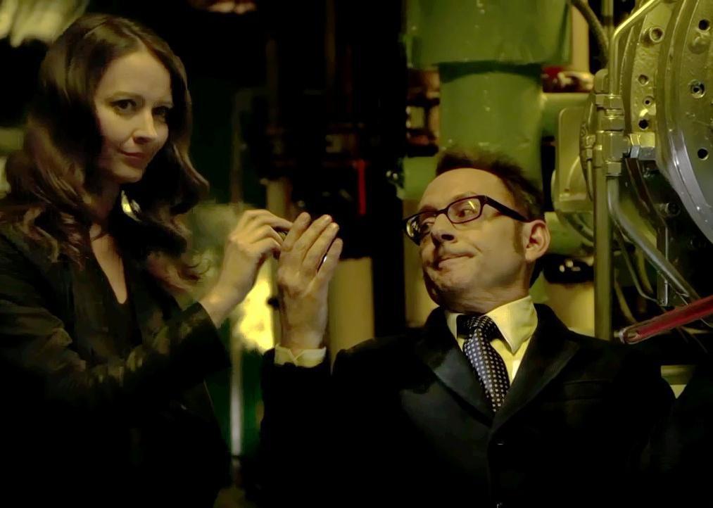 A woman hands something to a man in a suit in a boiler room.