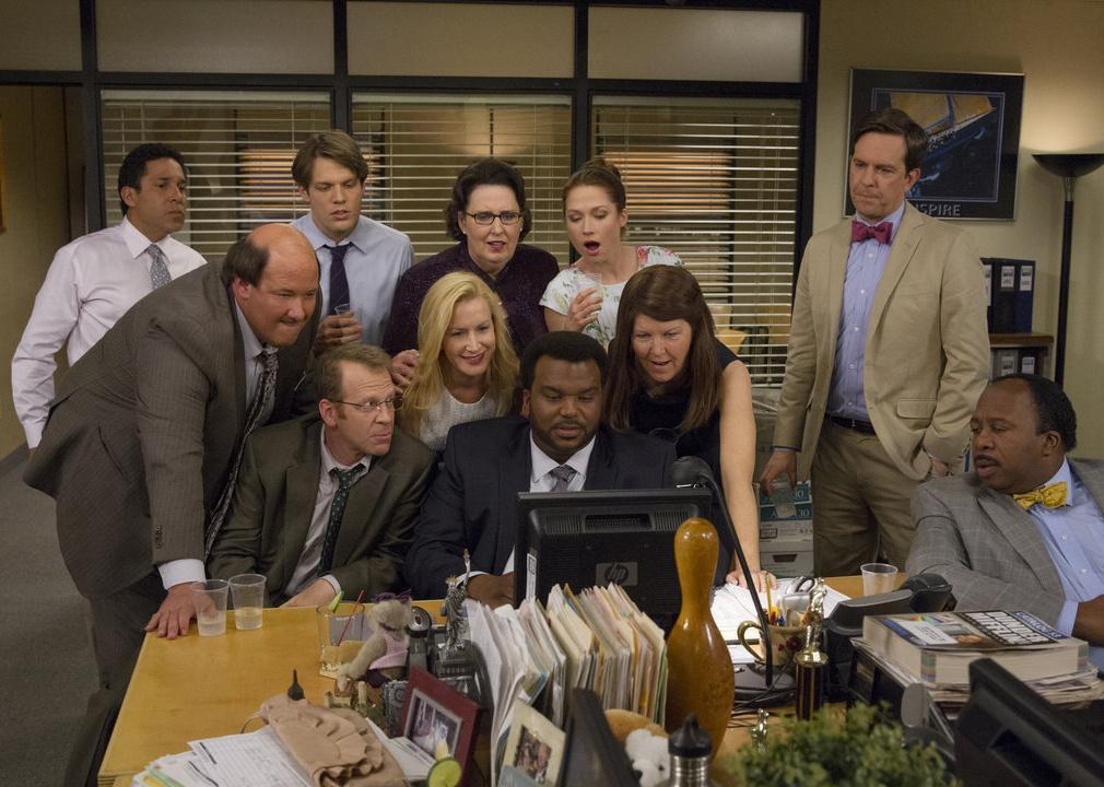 The cast of The Office stands together looking at a computer screen.