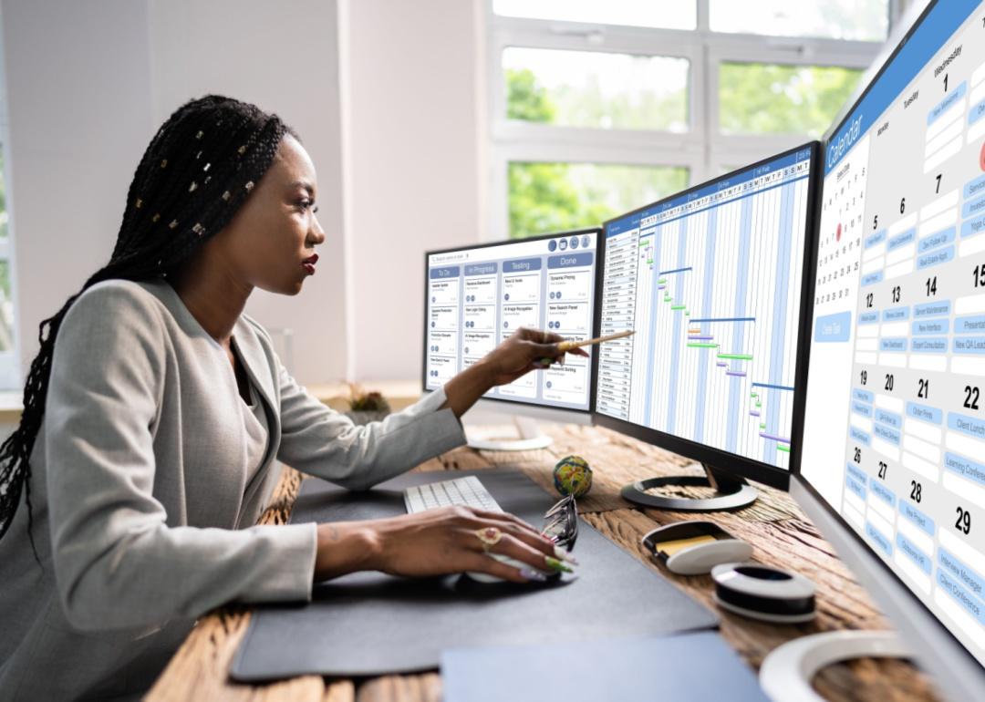 A person sitting at a desk with three screens open to different calendars.