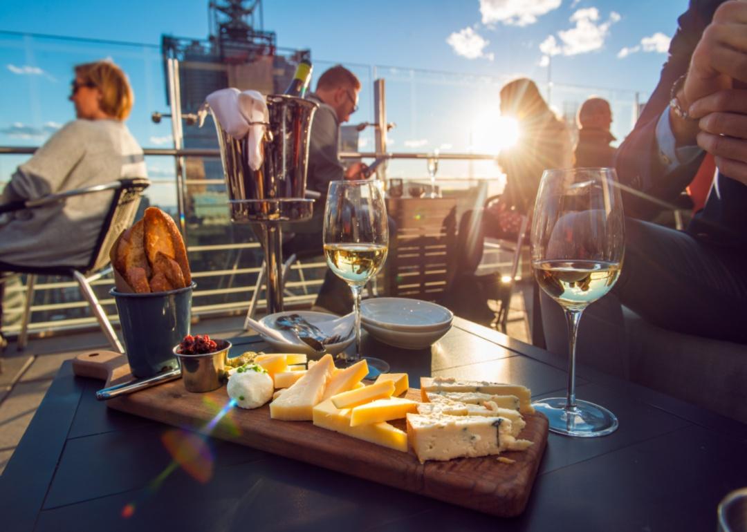 A cheese board and wine on a patio full of people.