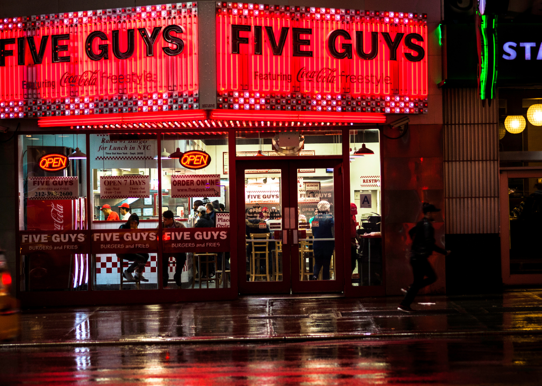 A crowded Five Guys restaurant with a red lit up sign.