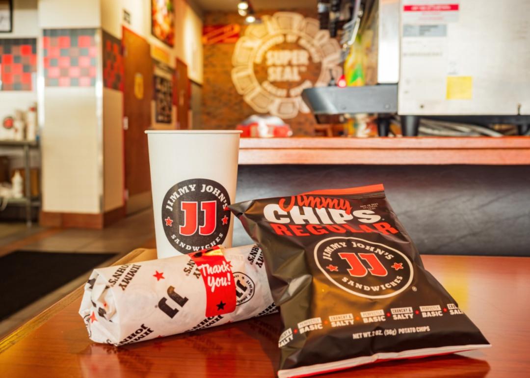 A Jimmy John's sandwich, bag of chips, and a drink.