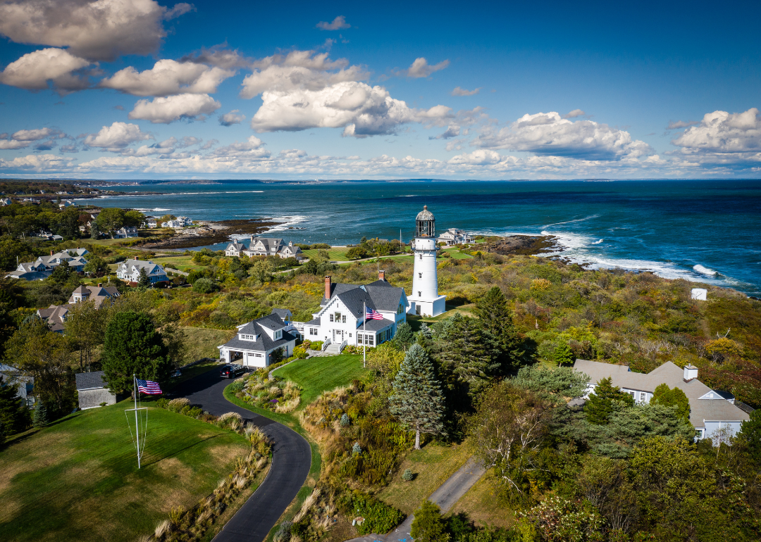 An aerial view of a lighthouse and homes near the water.
