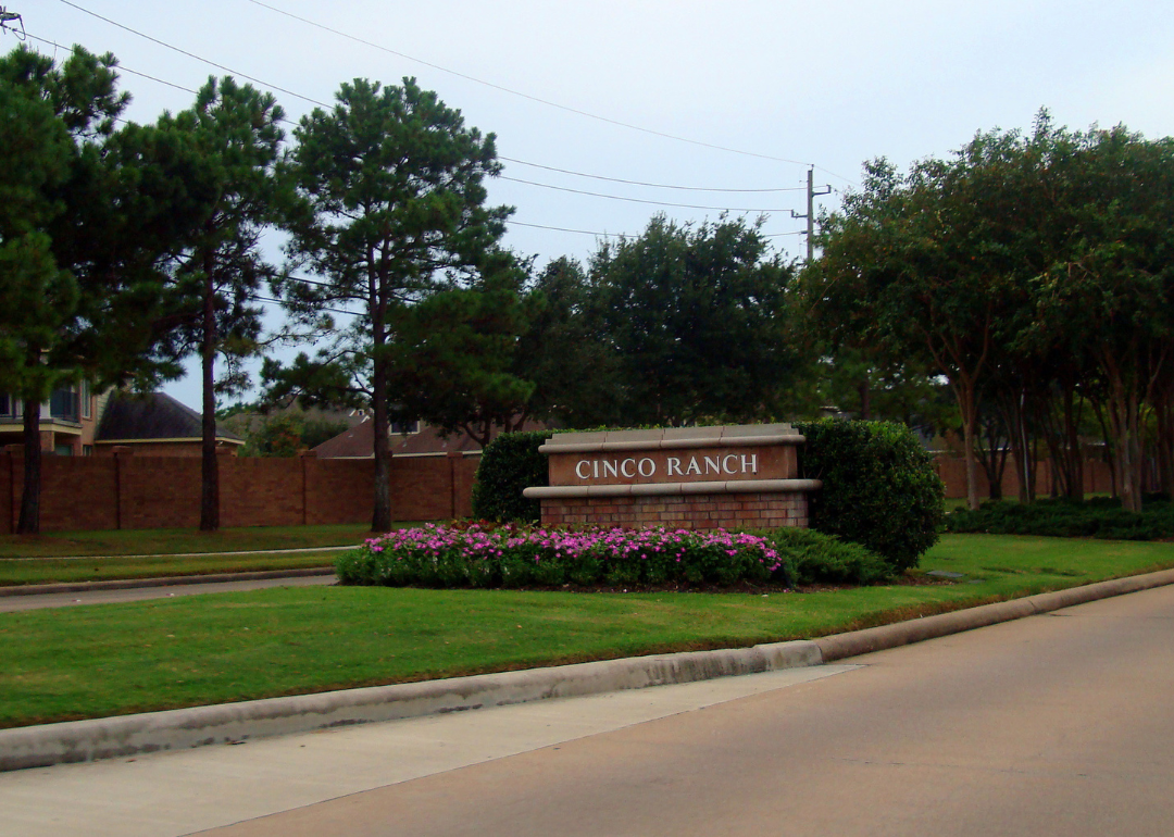 A road entering Cinco Ranch with homes behind a brick wall.