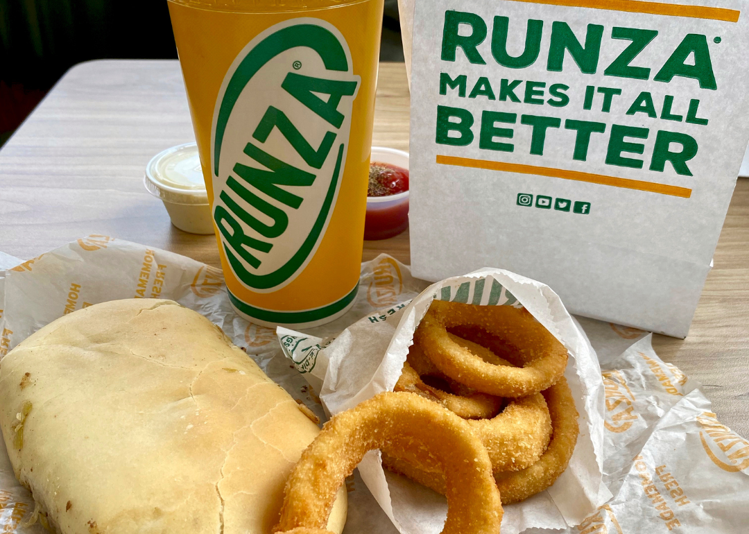 A stuffed sandwich, onion rings and a yellow drink cup with a Runza bag.