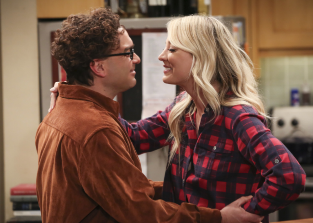 Kaley Cuoco and Johnny Galecki lean in for a kiss smiling.