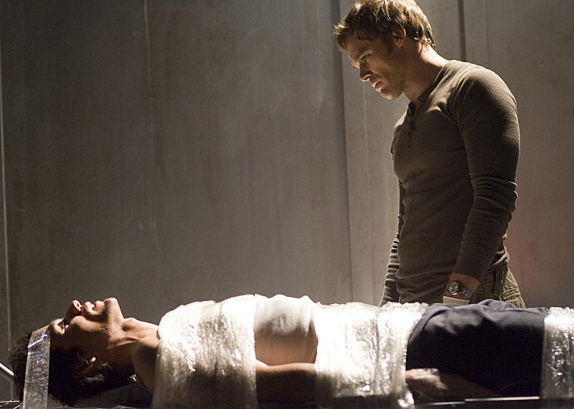 Michael C. Hall stands over a person tied to a table.