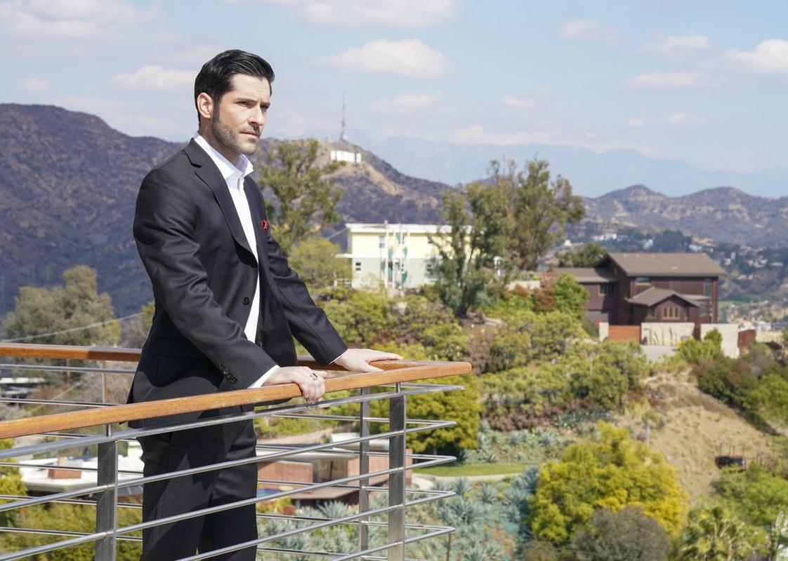 A man in a black suit stands on a rooftop balcony.