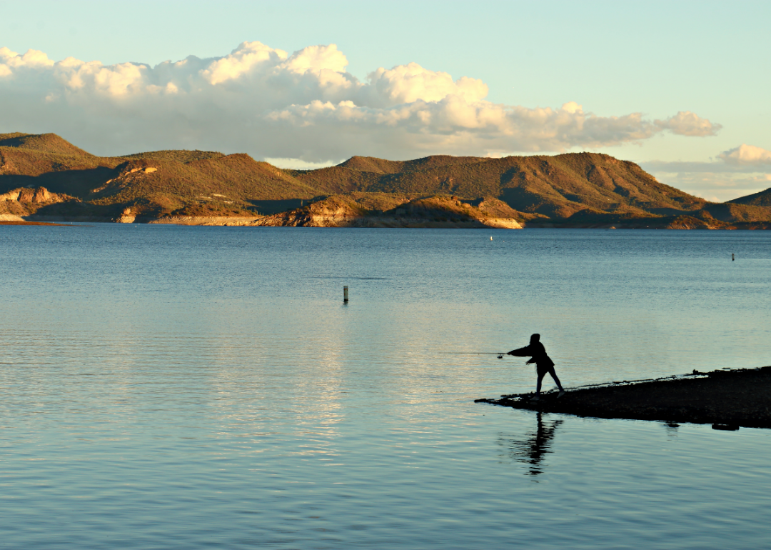 A person casting a fishing line into water with mountains in the background. 