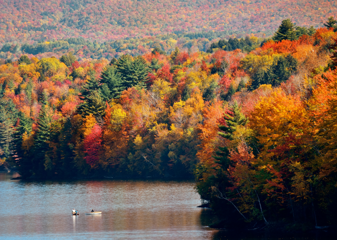 A distant view of a couple of small fishing boats surrounded by autumnal forest. 