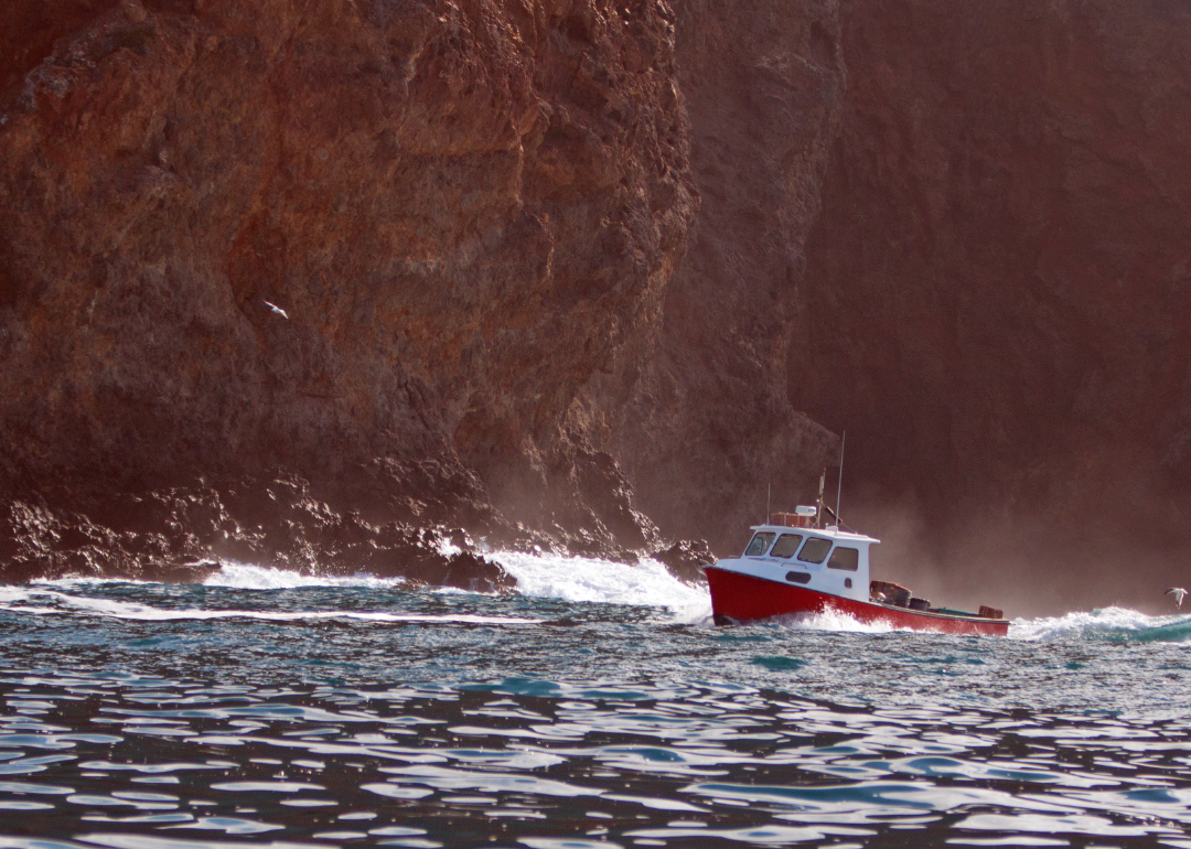 A fishing boat in slightly choppy waters alongside a rocky cliff. 