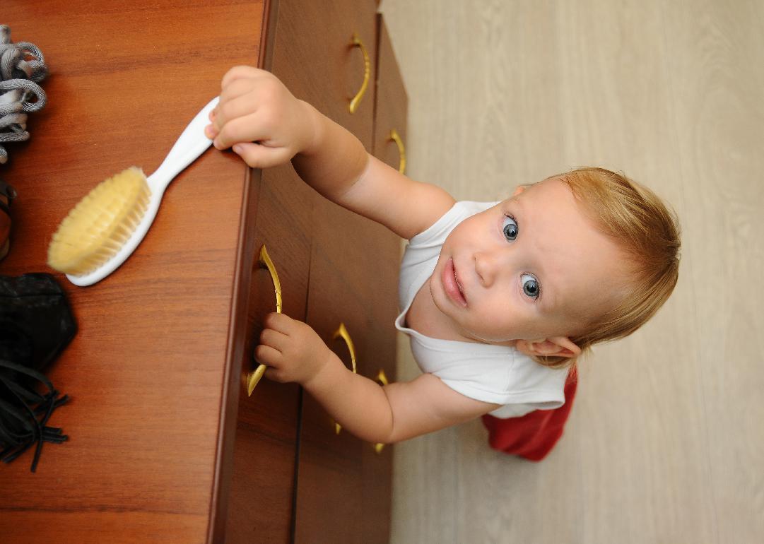 An infant looking up, holding onto the handle of a dresser drawer.