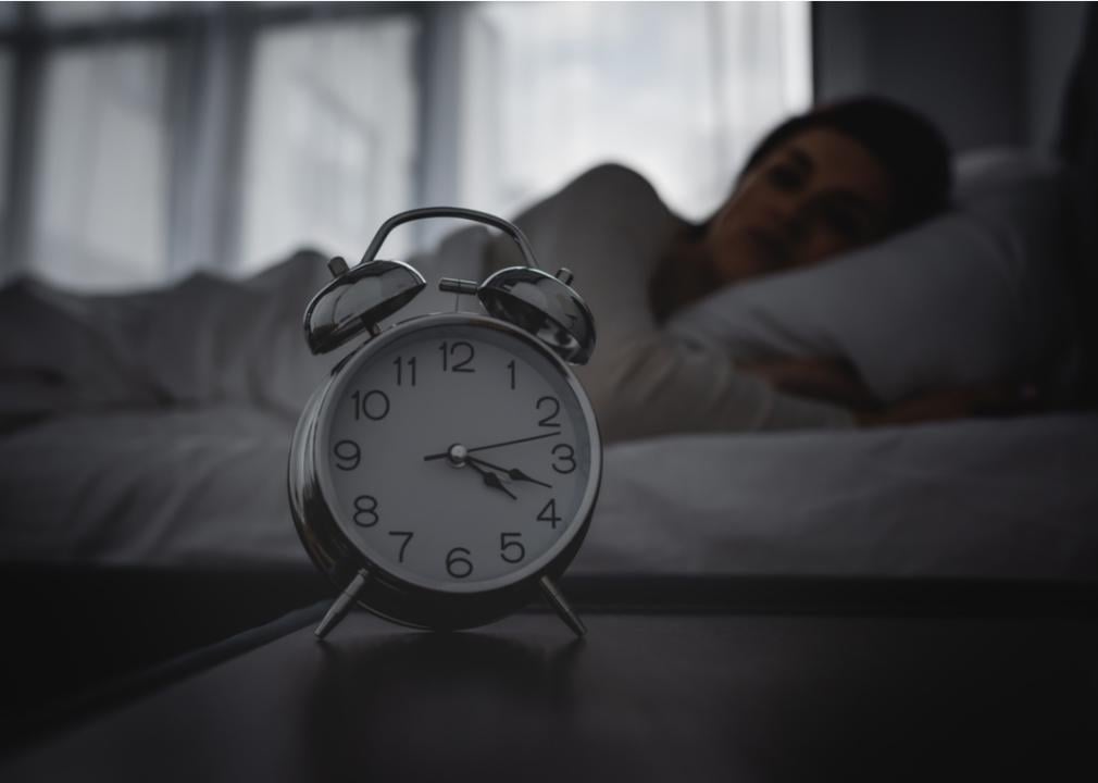 Clock in the middle of the night and woman awake in bed in background.