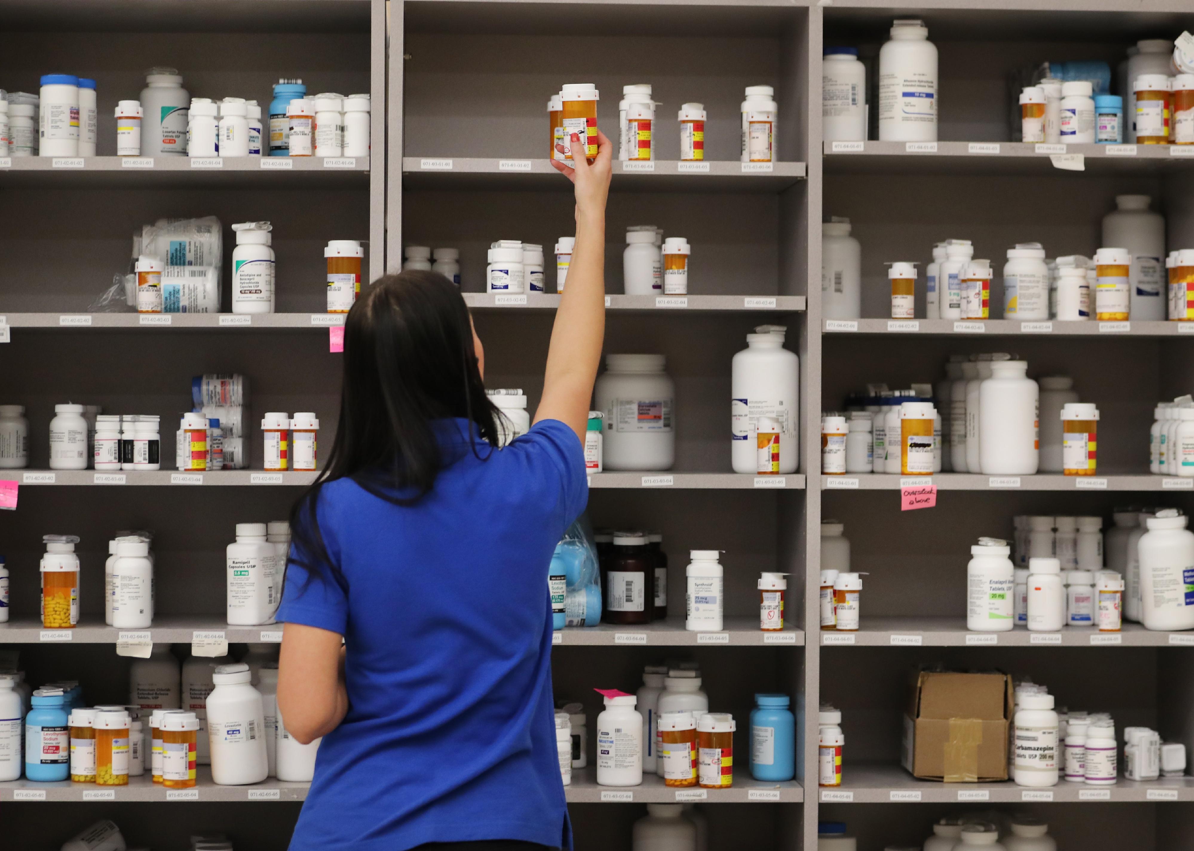 A pharmacy technician grabs a bottle of drugs off a shelve