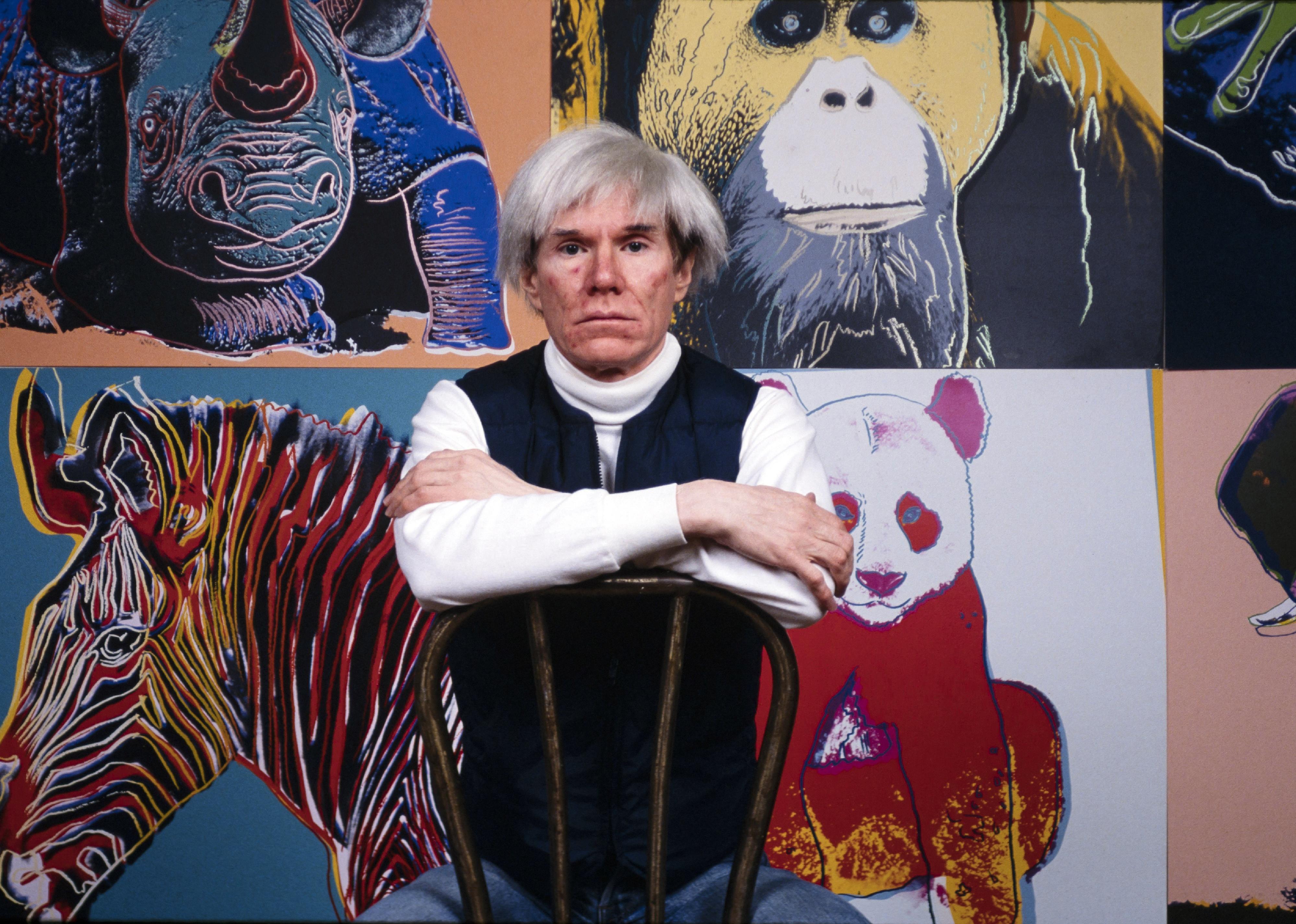  Andy Warhol sits in front of several paintings in his 'Endangered Species' at his studio.