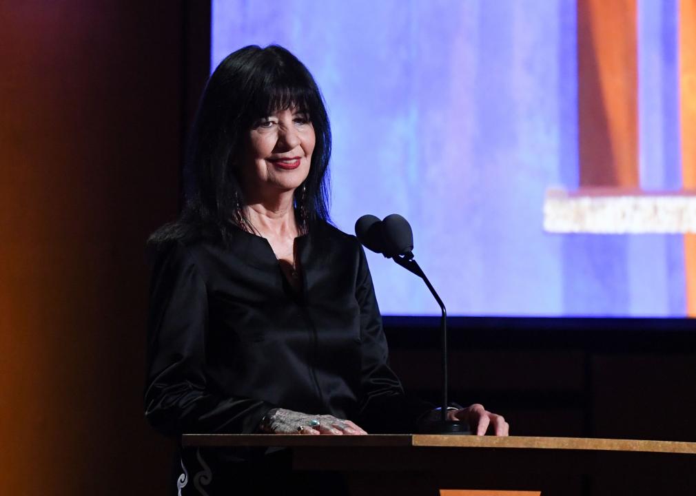 Joy Harjo on a stage behind a podium with mics set up in front of her.