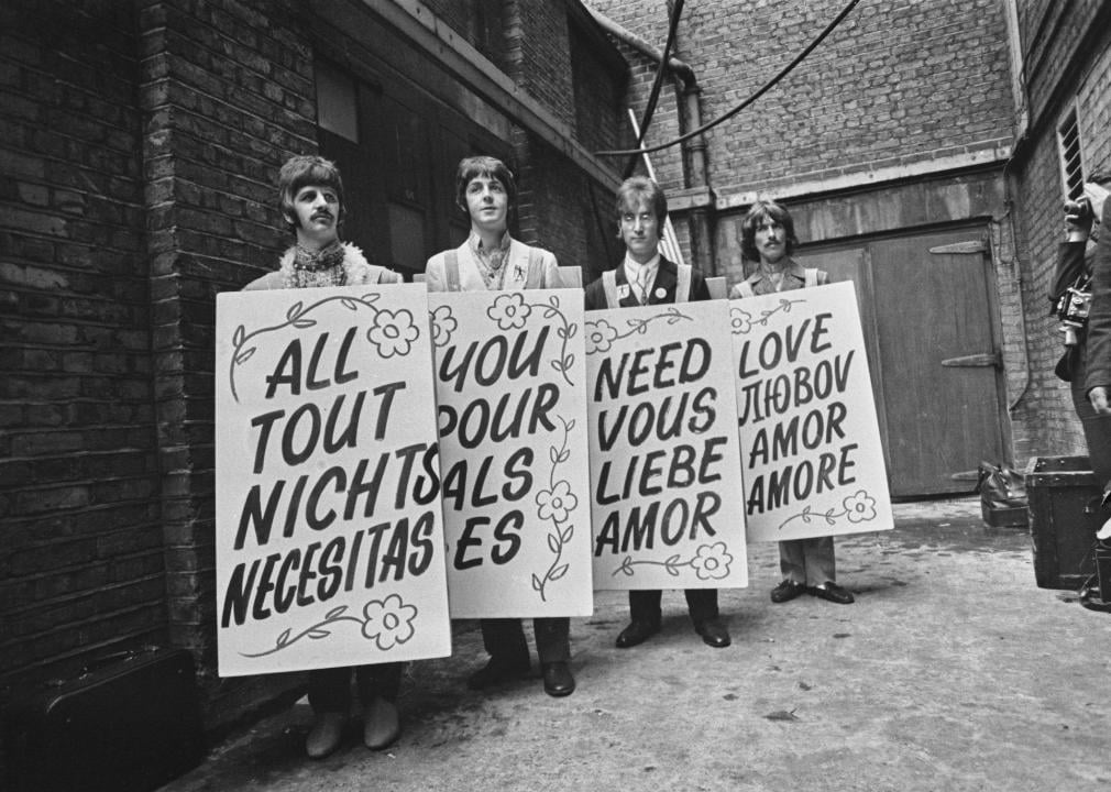 The Beatles hold up sandwich boards in different languages.