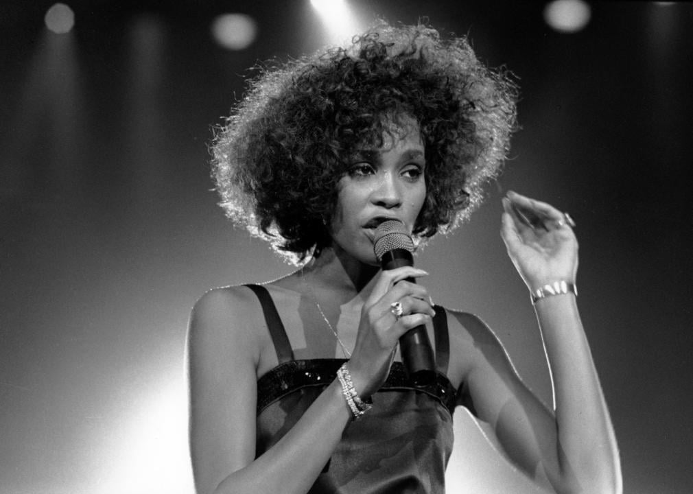 Whitney Houston performing onstage in black dress.