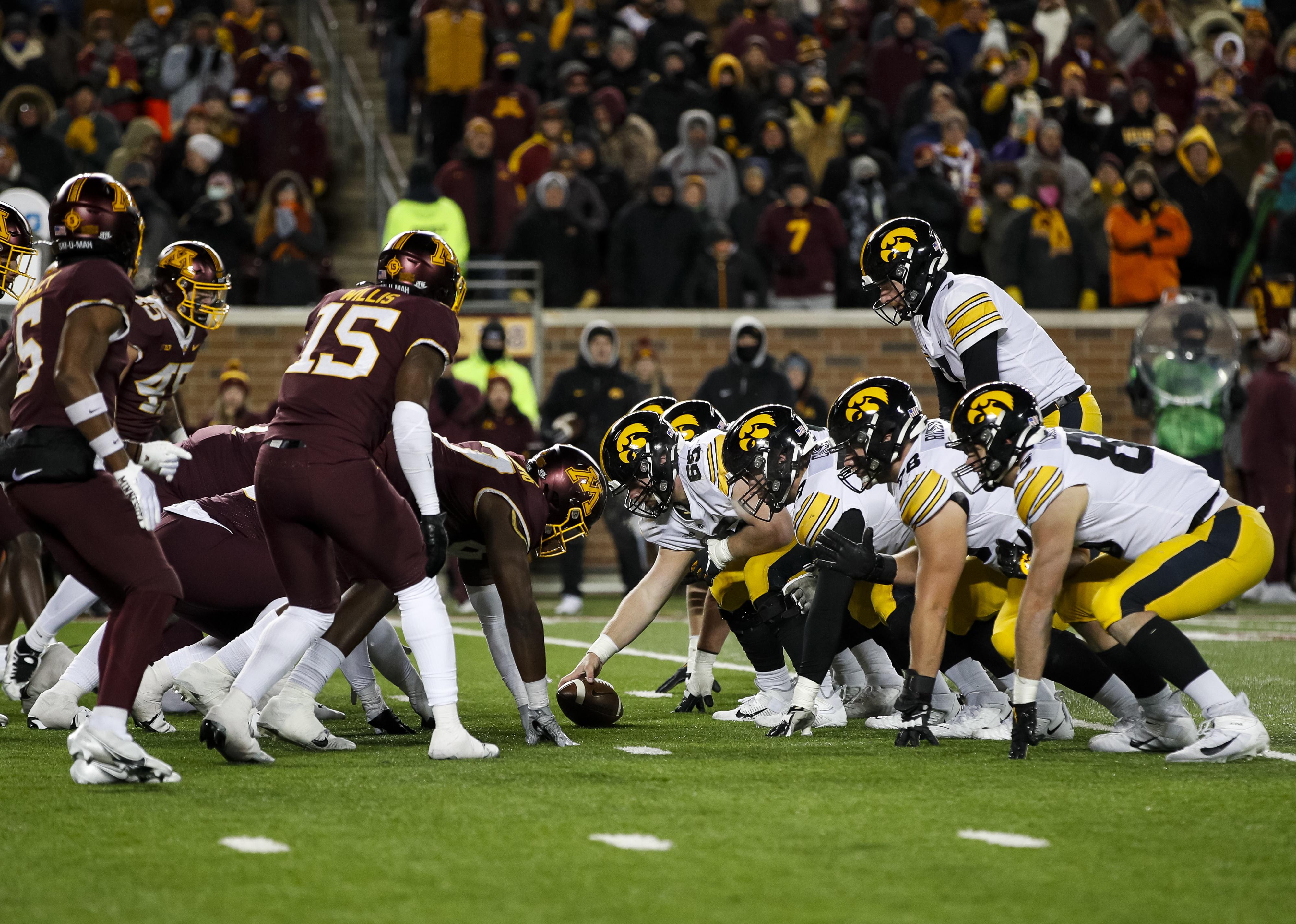 Members of the Iowa Hawkeyes and Minnesota Golden Gophers line up at the line of scrimmage.
